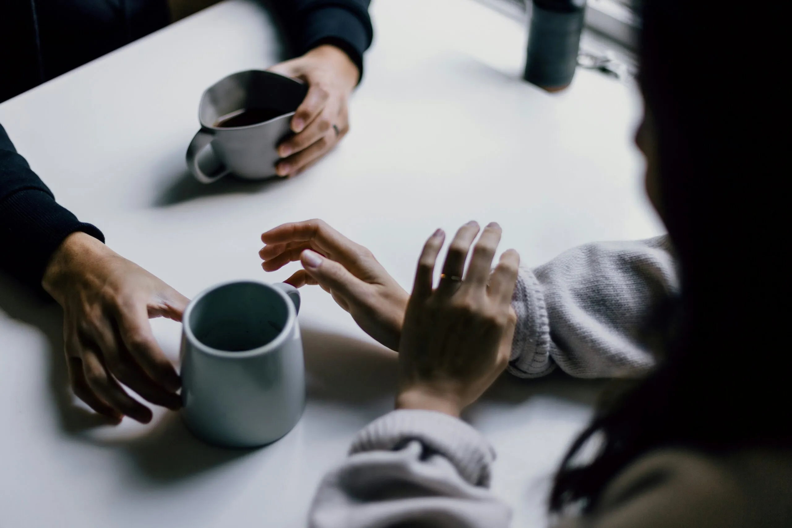 The hands of two people at a table with coffee cups.