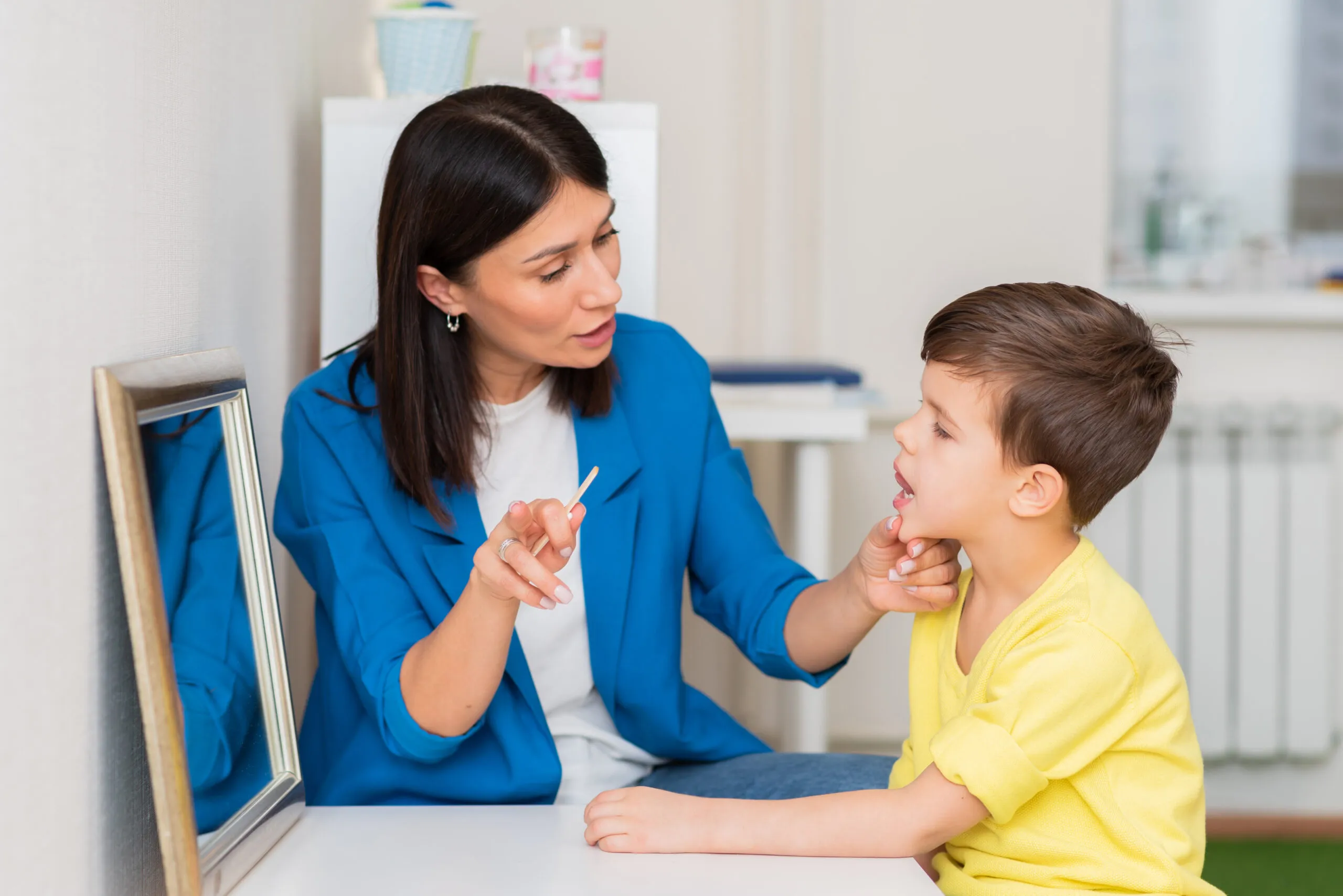 Woman speech therapist helps a boy correct the impediment of his speech
