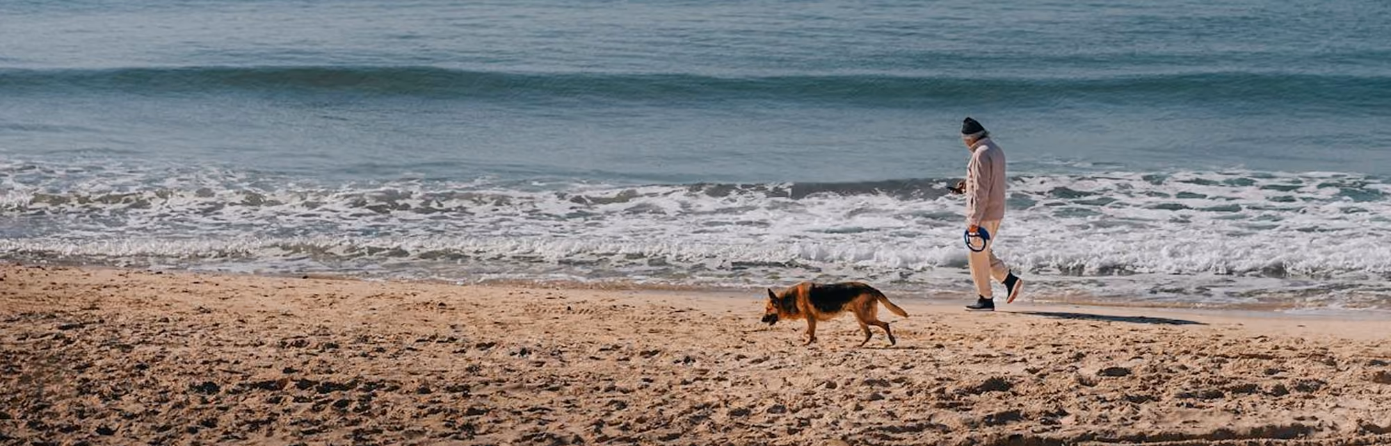 man walking along beach with dog