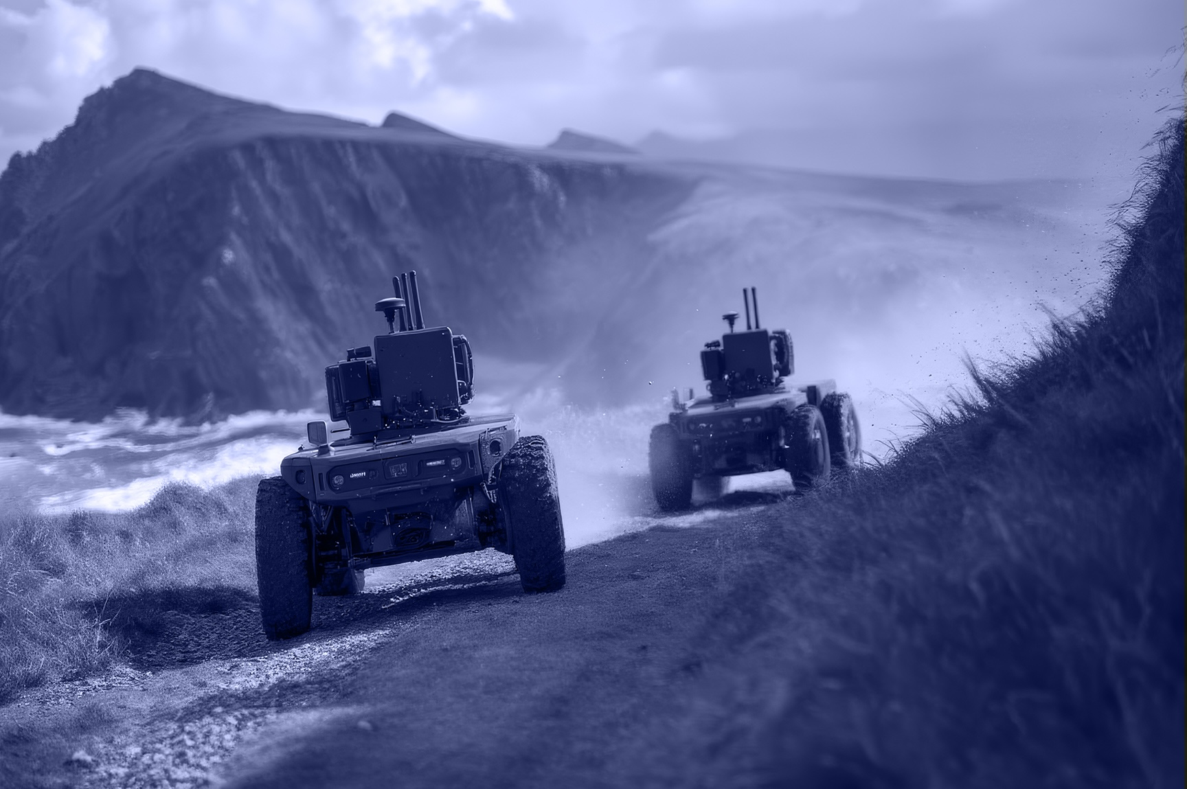 Two small robots with cameras navigating a rocky coastal path near cliffs and ocean waves.
