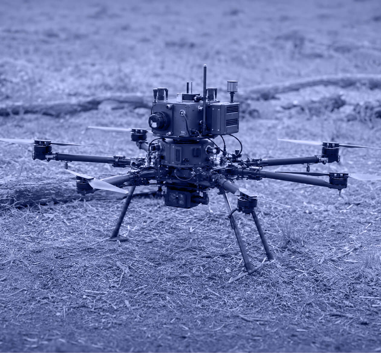 Black multi-rotor drone with eight propellers and sensors on forest floor.