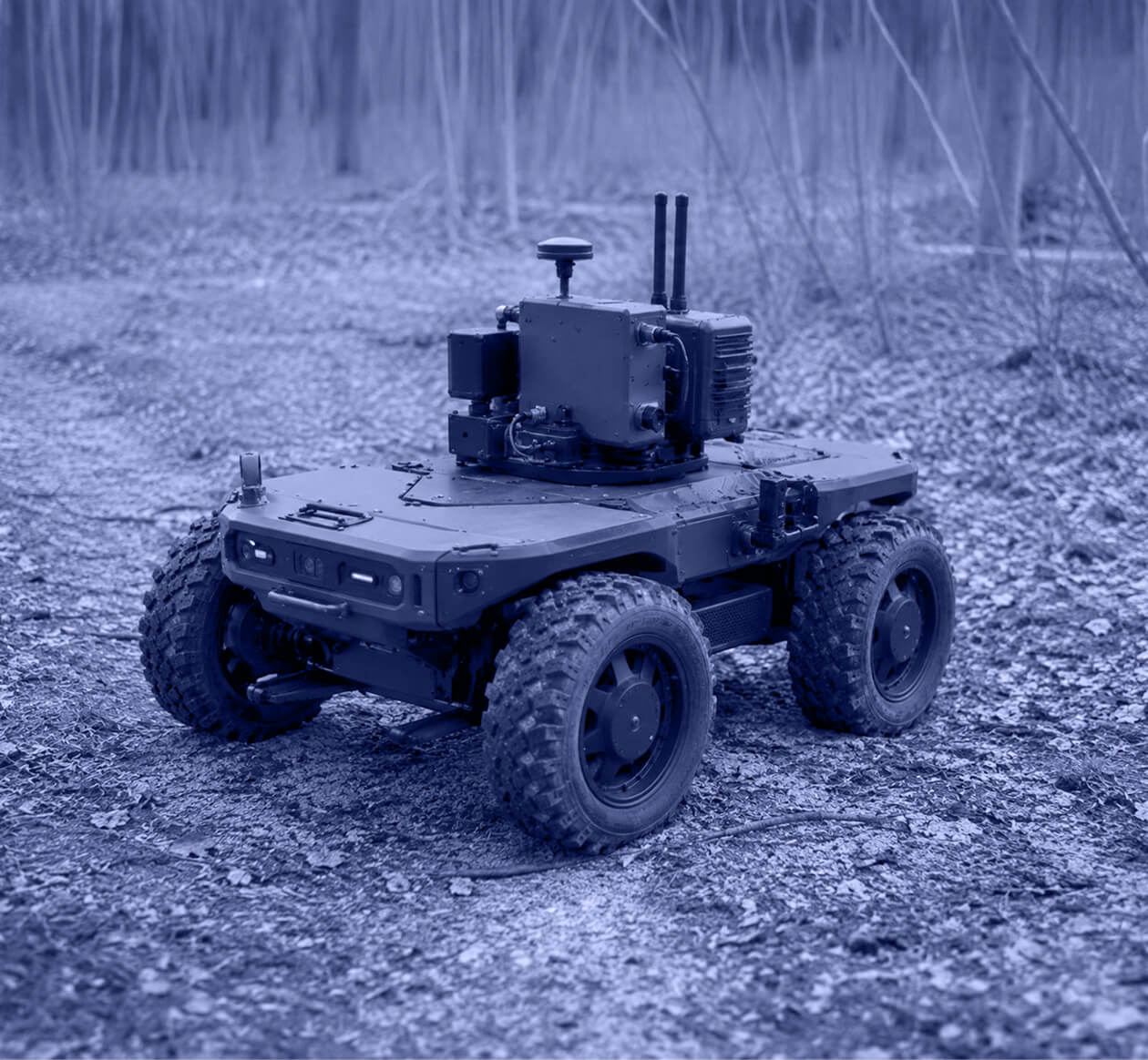 Four-wheeled autonomous vehicle with sensors on dirt-covered forest ground.