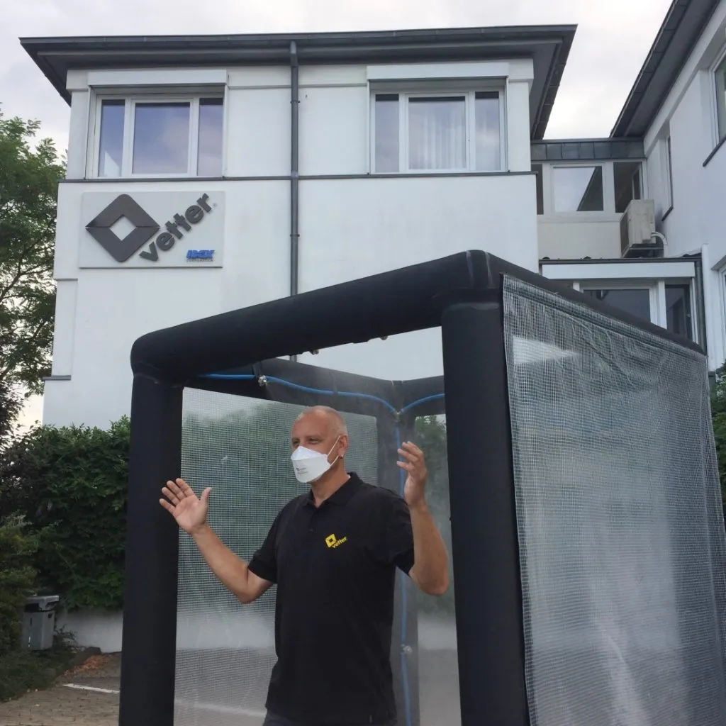 A photograph of a man demonstrating a Vetter  decontamination/ pop-up shower