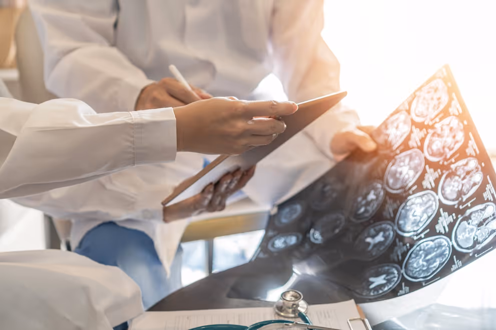 Two doctors reviewing brain scans and taking notes on a clipboard in a bright room.