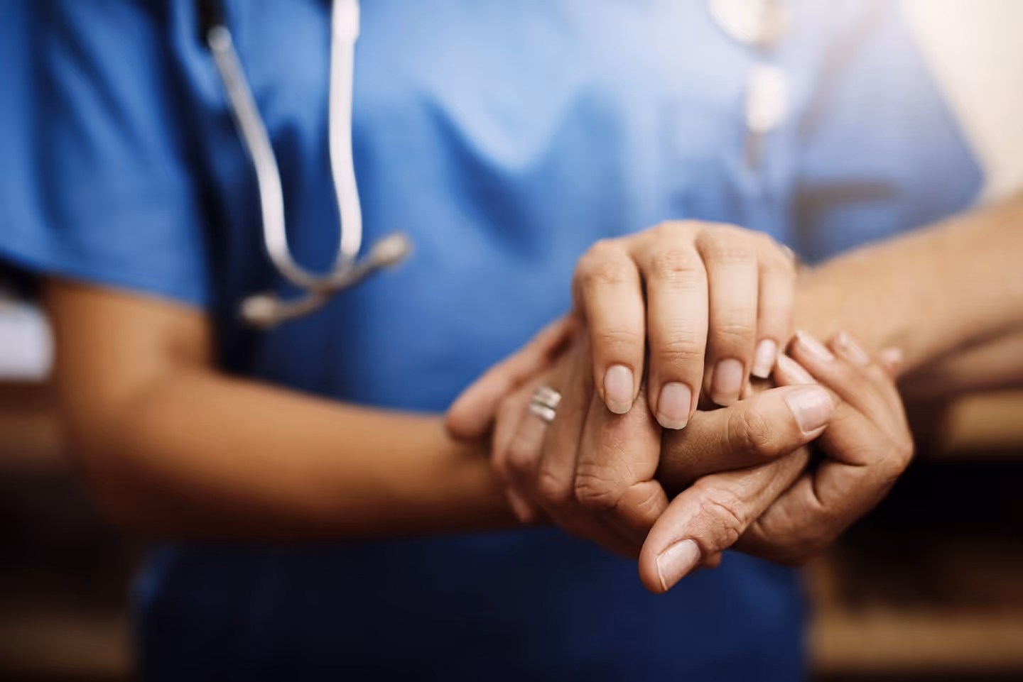 Healthcare worker in blue scrubs gently holding a patient's hand for support and comfort.