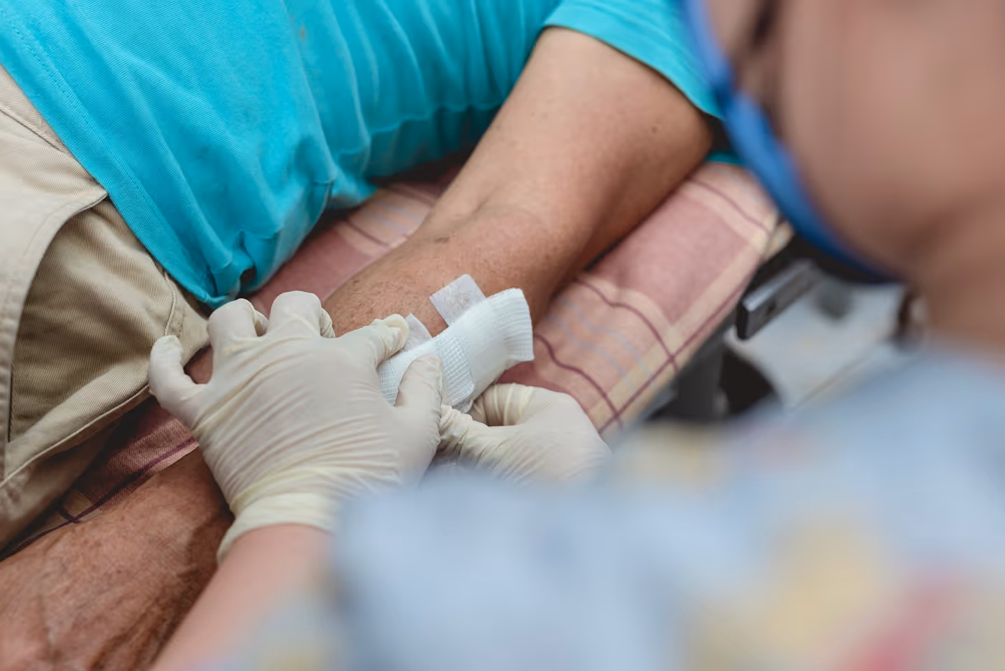 Healthcare worker wearing gloves applying a bandage to a man's arm on a padded surface.