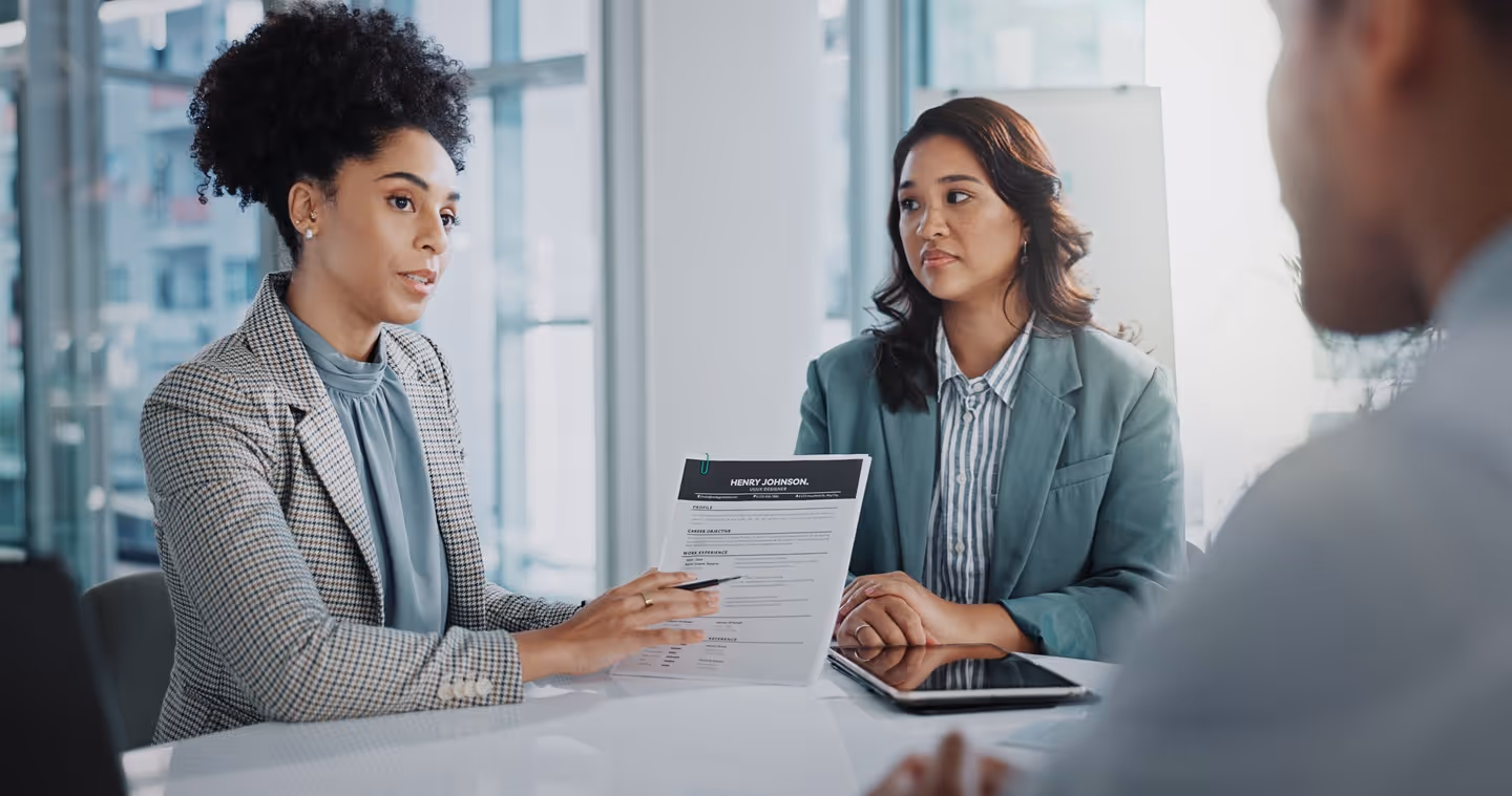 Two women in a job interview discussing a resume held by one of them at a modern office table.