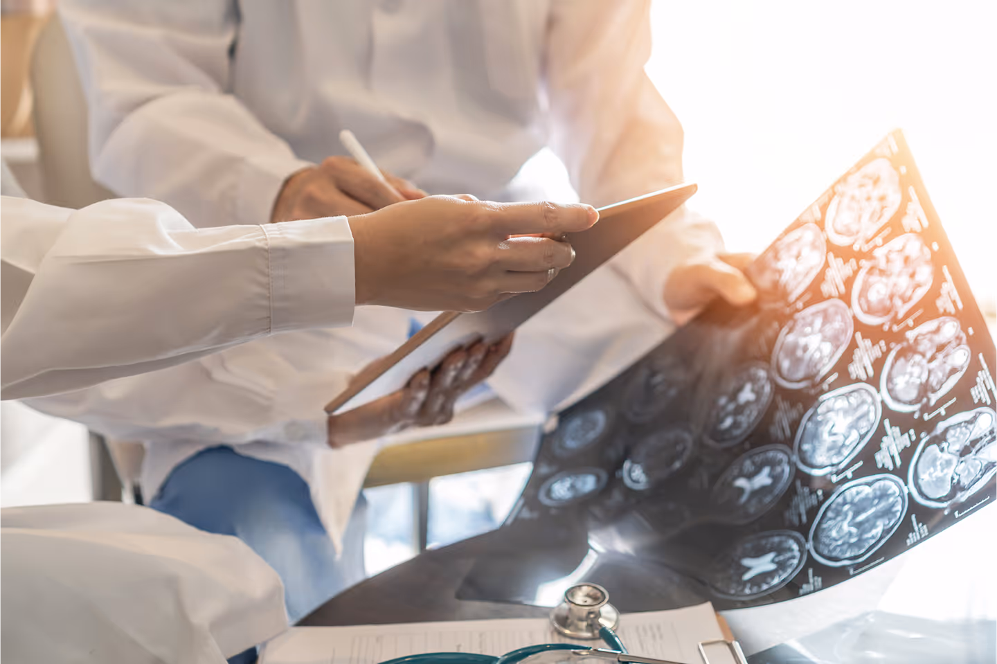 Two doctors reviewing brain scan images and notes on a digital tablet together at a desk.