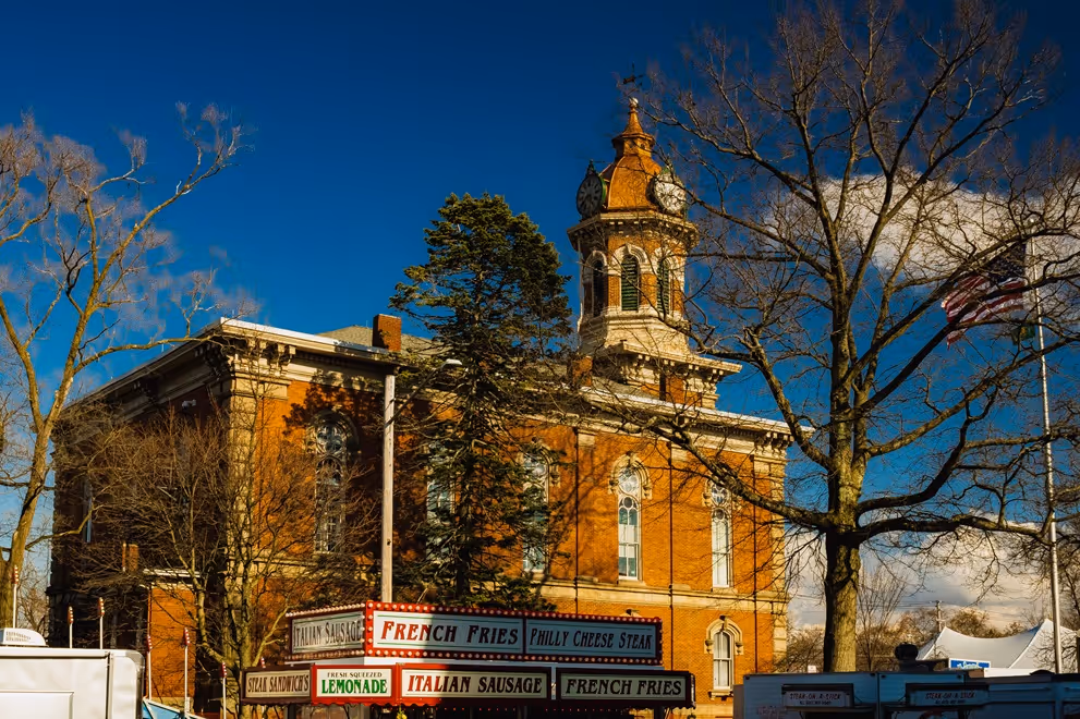 Historic brick building with clock tower and food stands offering French fries, Italian sausage, and lemonade.