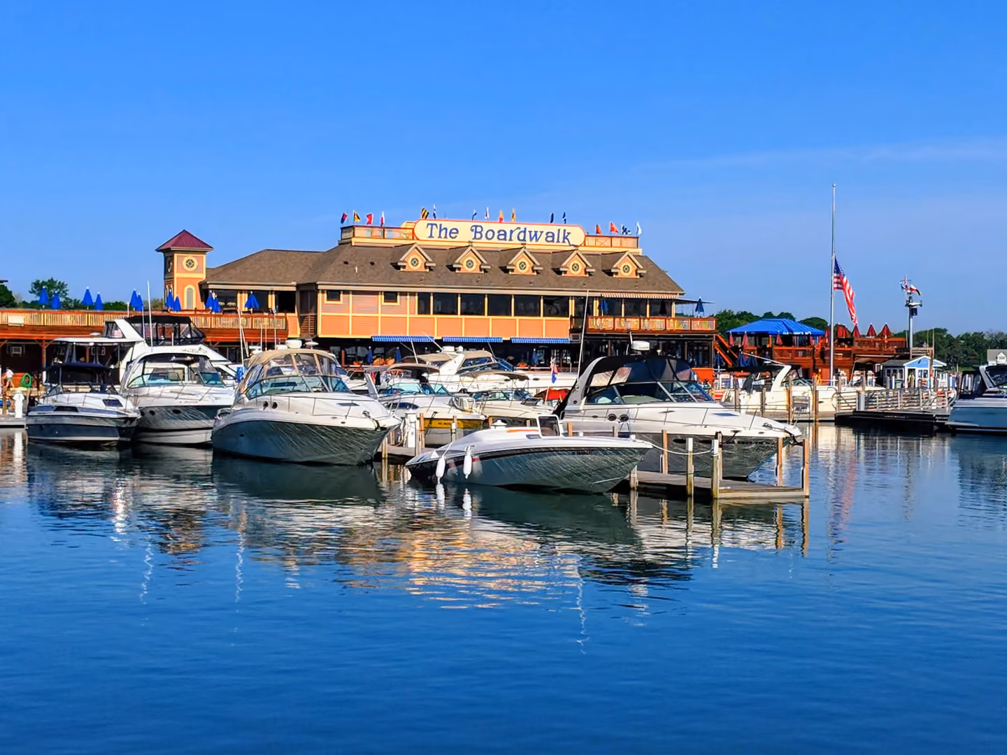 Boats docked in calm water in front of a large boardwalk building under clear blue sky.