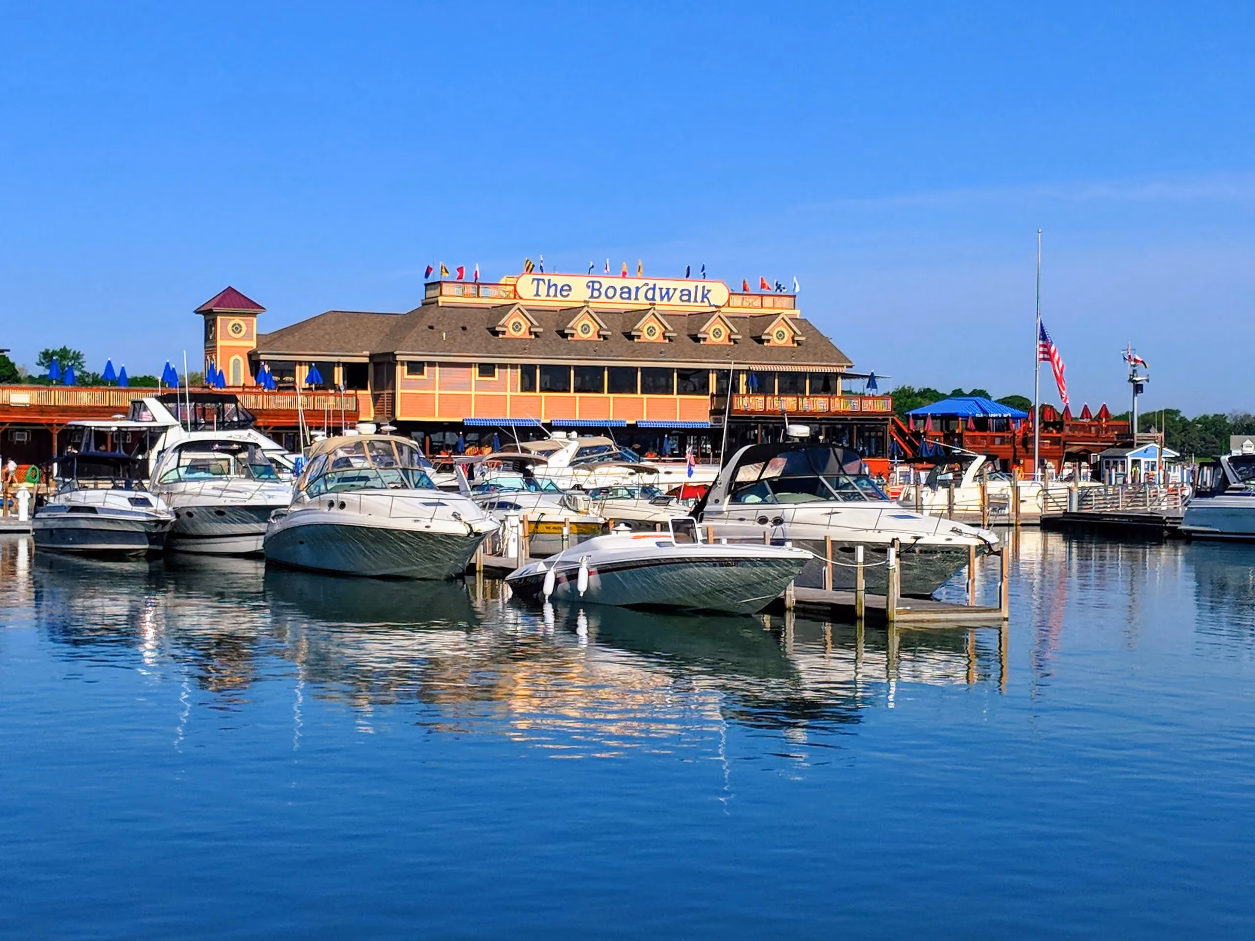 Boats docked in calm water in front of a large boardwalk building under clear blue sky.