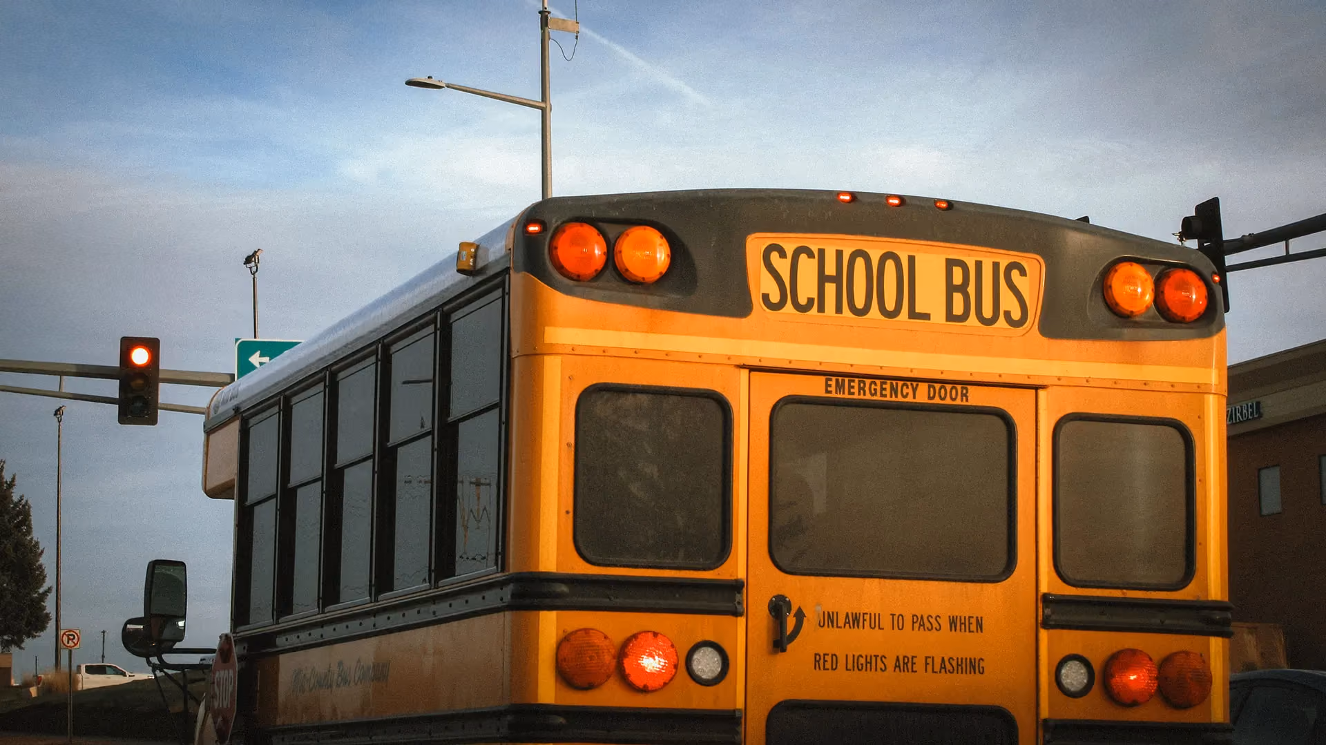 Rear view of a yellow school bus stopped at a red traffic light with warning lights on.