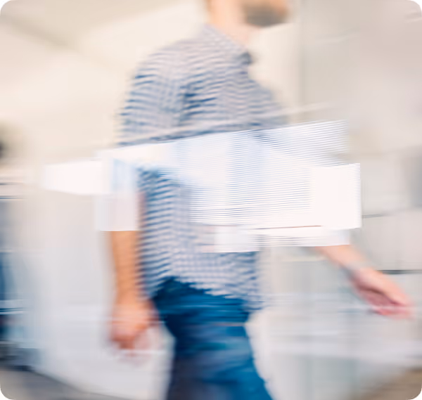 Blurred image of a person walking indoors wearing a striped shirt and jeans.