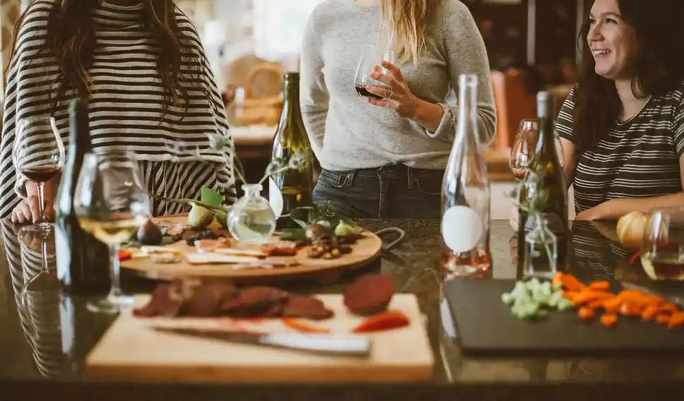 Three women standing around a kitchen island with wine glasses and charcuterie boards with food.