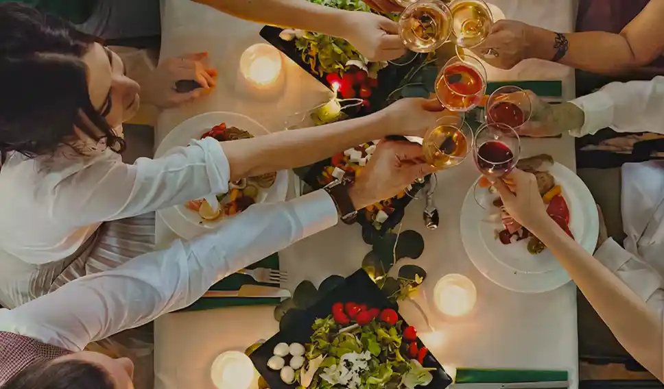 Top view of people toasting with wine glasses over a candlelit dinner table with food platters.