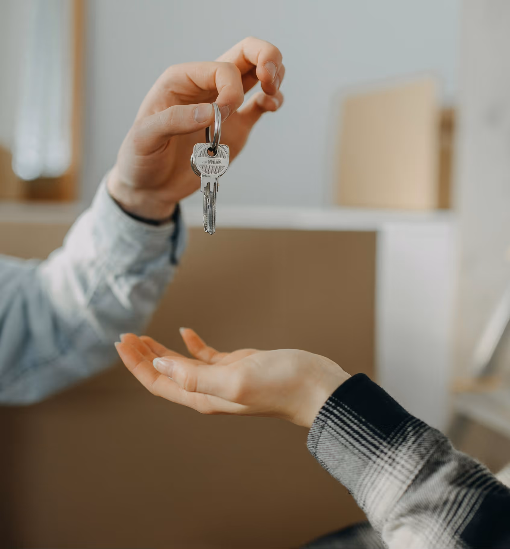 Hand passing a key to another open hand in front of cardboard boxes indoors.