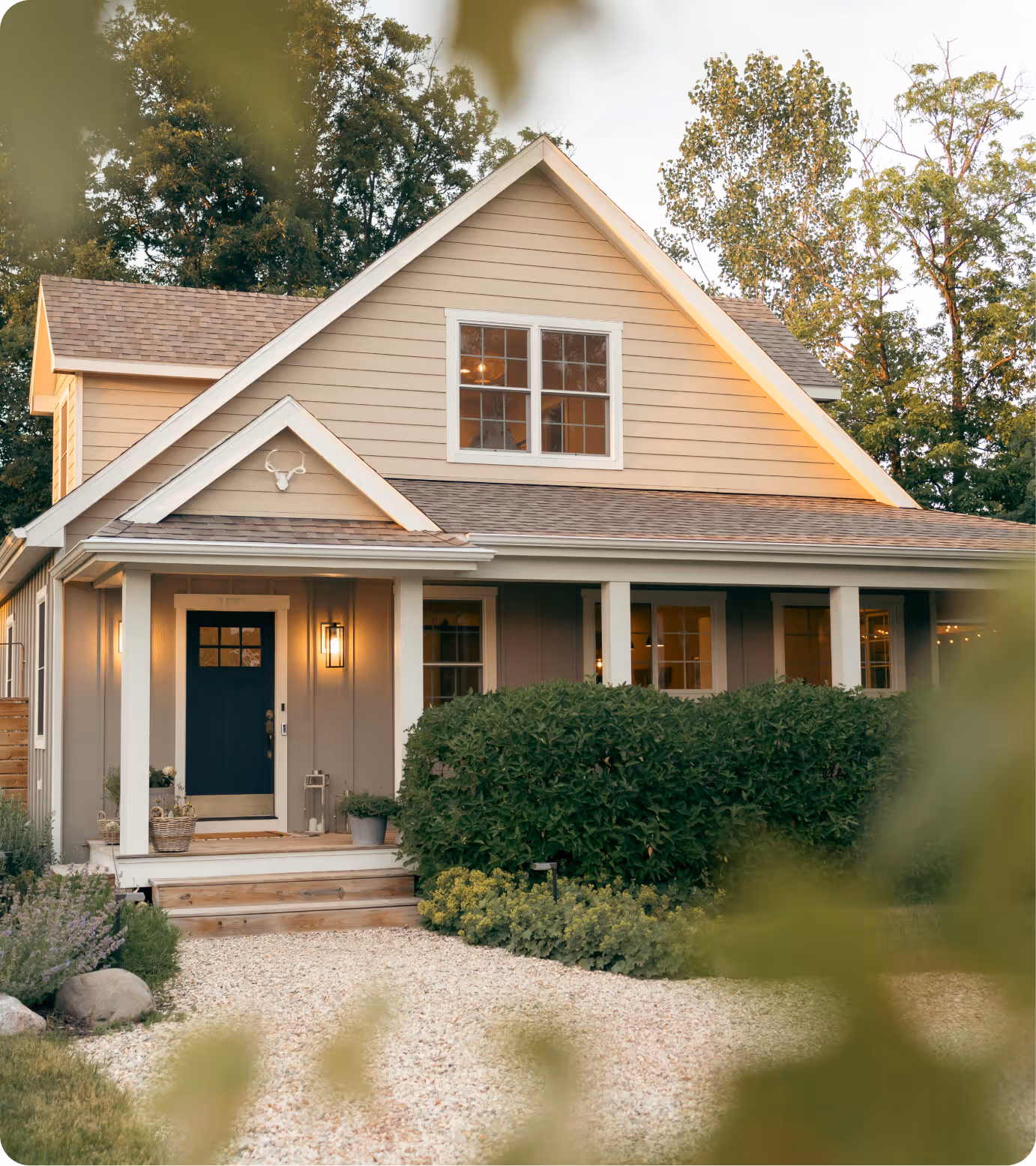 Two-story beige house with blue front door, porch, shrubs, and gravel pathway in front yard.