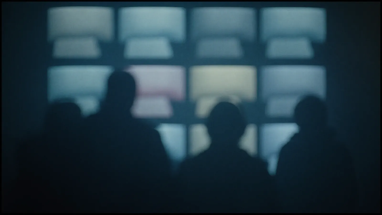 Out of focus wall of monitors glowing in a dark control room