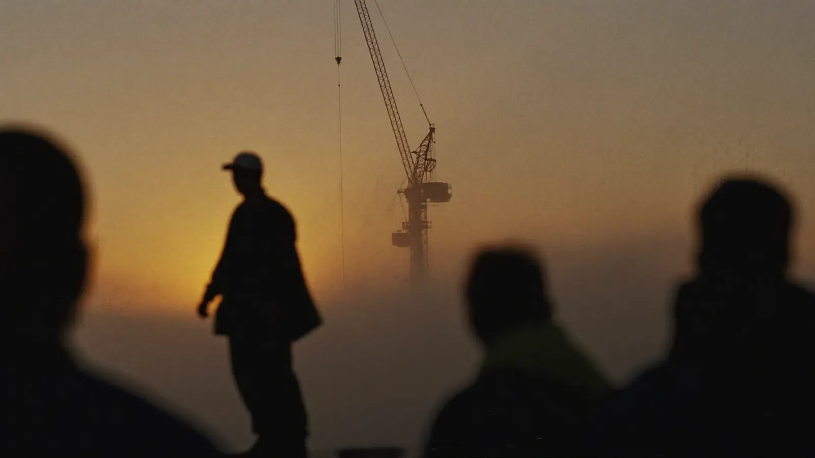 Tower crane and silhouetted workers in sunrise haze