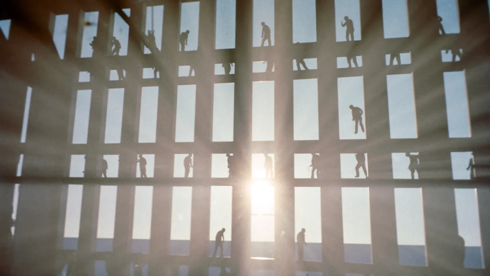 Workers silhouetted on a high steel frame against a bright sky