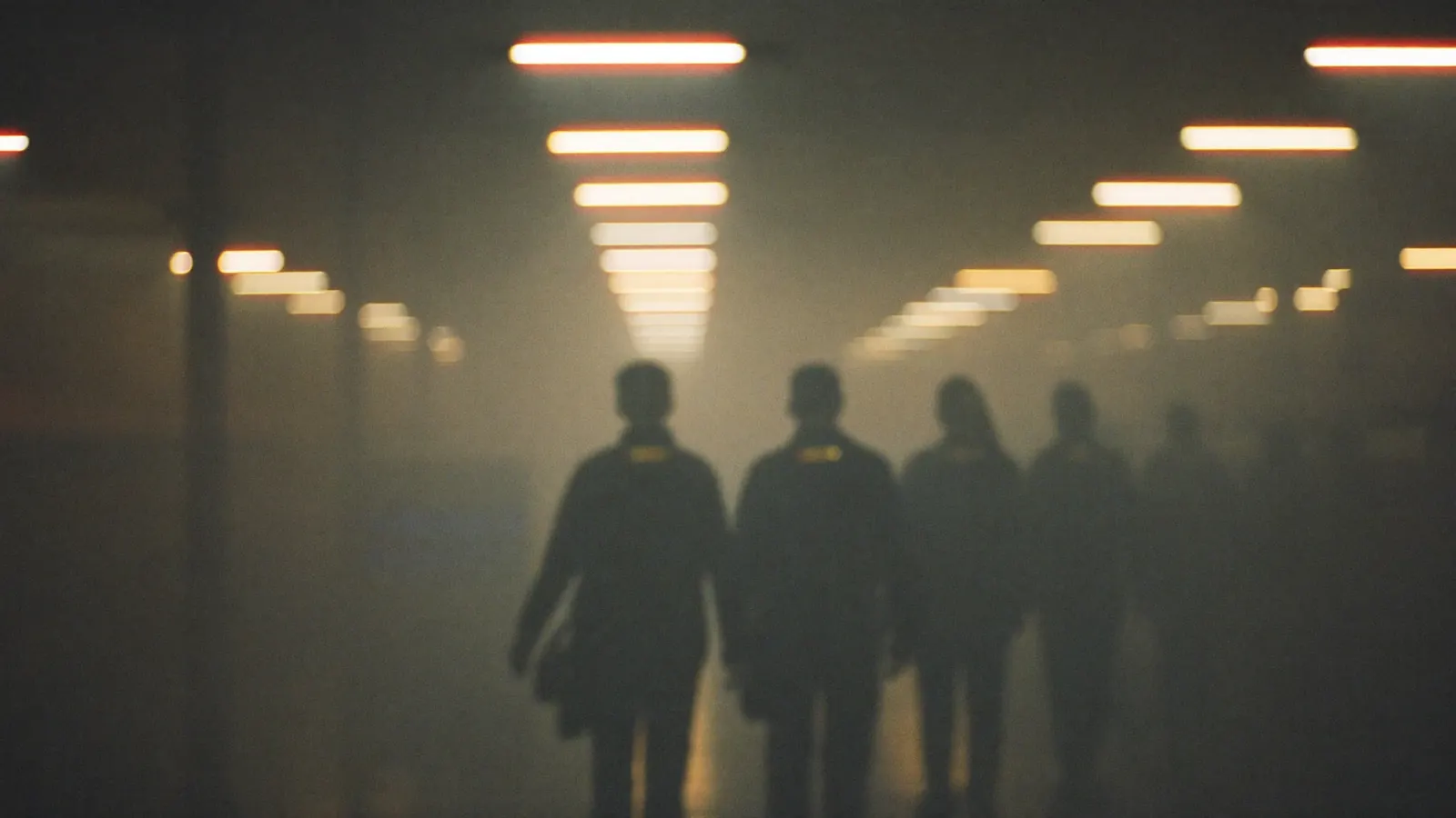 Warehouse corridor with receding overhead lights and walking silhouettes, soft focus