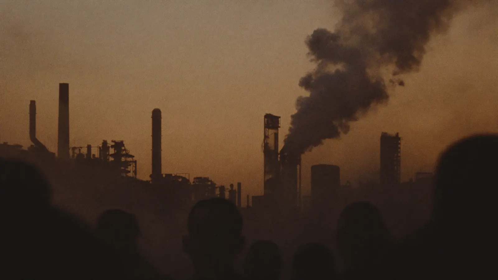 Refinery towers and rising smoke silhouetted against a dusk sky