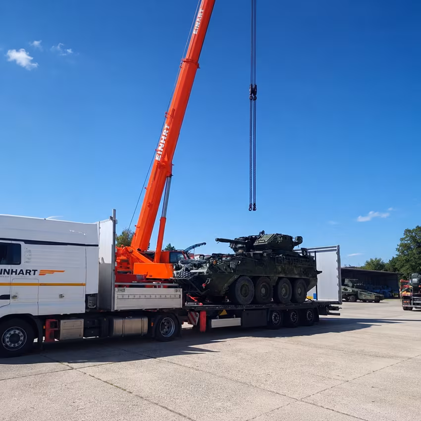 Heavy tracked vehicle being transferred by crane onto a low-loader