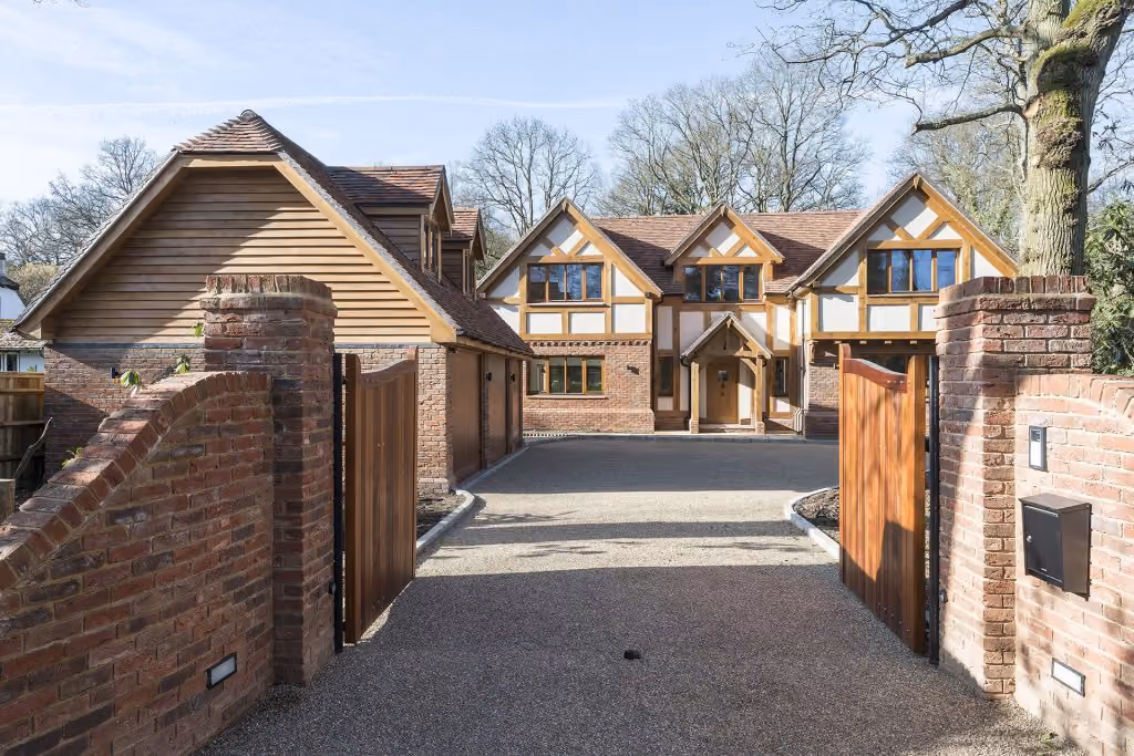 Large brick and timber house with wooden gates open to a gravel driveway.