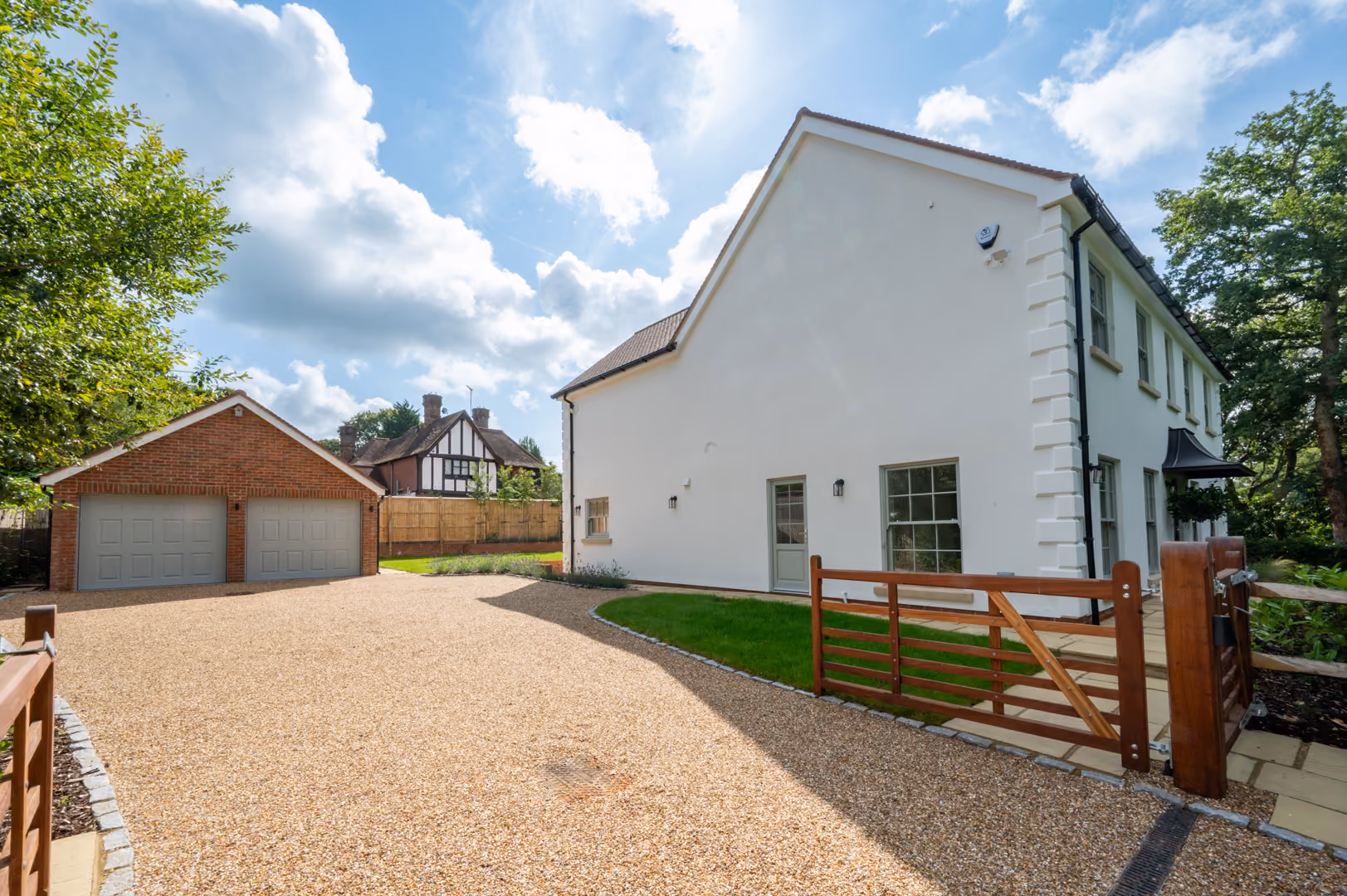 Gravel driveway leading to a white two-story house and separate brick garage with two gray doors.