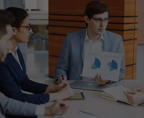 Man in glasses shows pie charts on paper during a business meeting with colleagues at table.