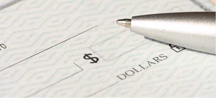 Close-up of a pen tip pointing at the dollar amount box on a blank check.