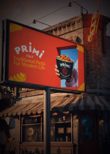 Outdoor billboard advertisement for Primi Italy featuring a hand holding a cup of pasta against a red background with the text 'Primi Italy Traditional Pasta For Modern Life' and pasta shapes in the corners.