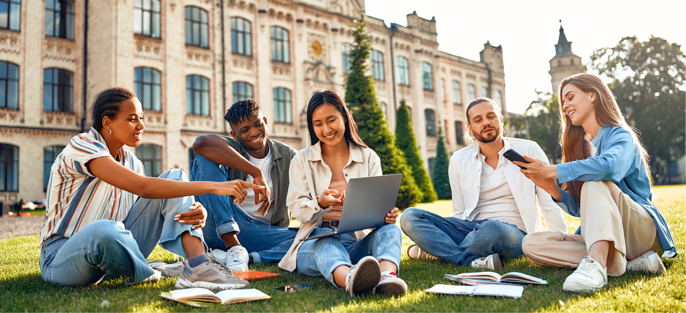 Diverse university students collaborate outdoors using laptop and notes during a campus study session together