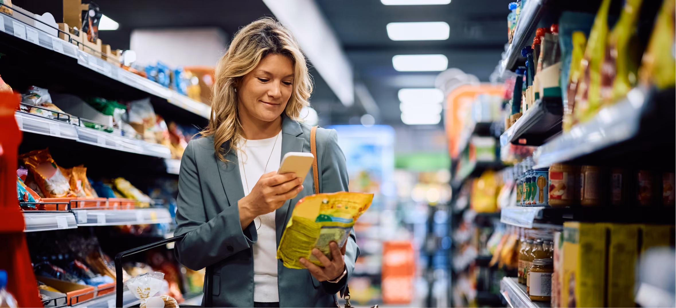 Professional shopper scans packaged food label with smartphone while comparing products in a supermarket aisle