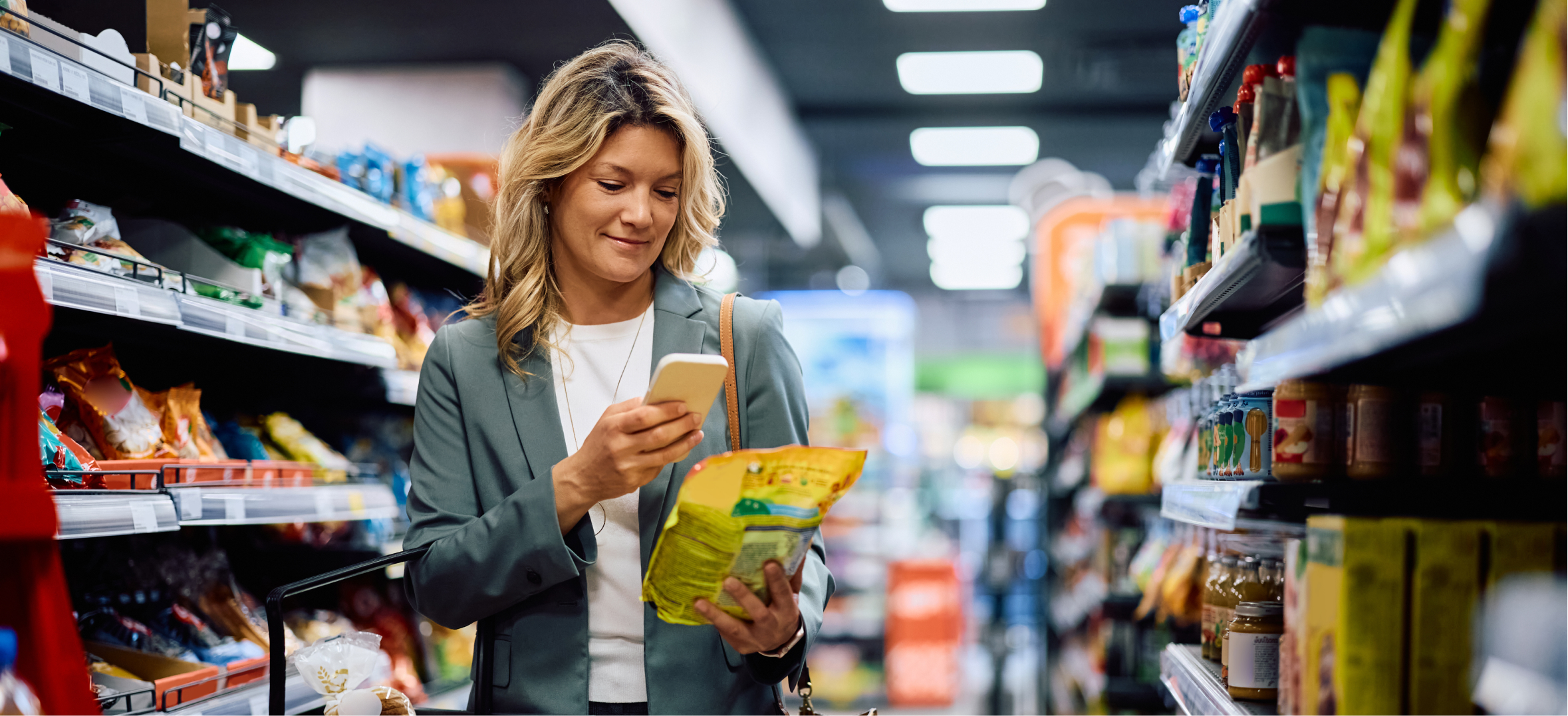 Professional shopper scans packaged food label with smartphone while comparing products in a supermarket aisle