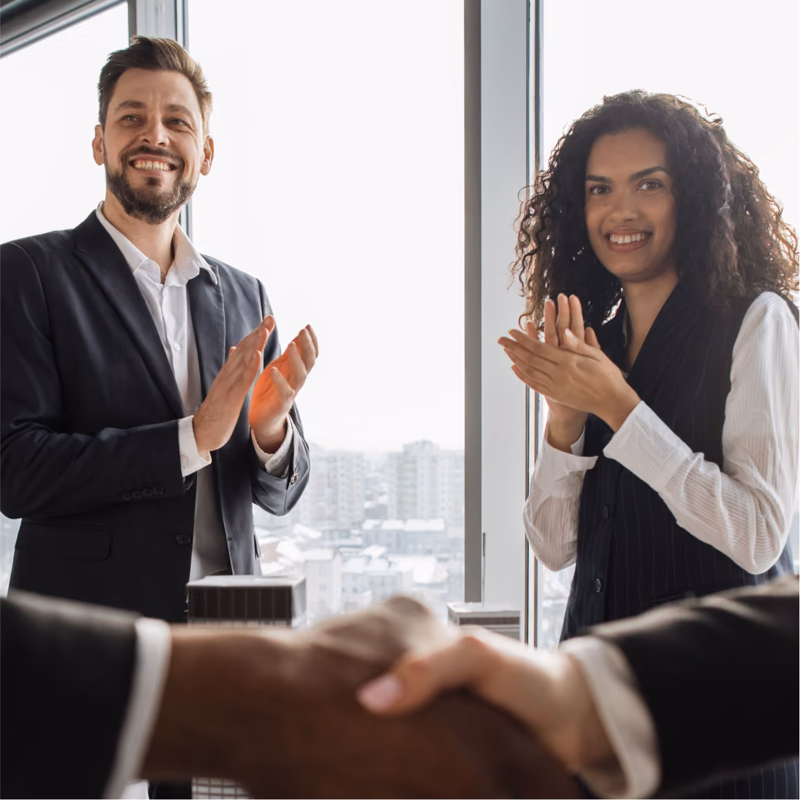 Business partners celebrate successful agreement with handshake while colleagues applaud in modern office sett