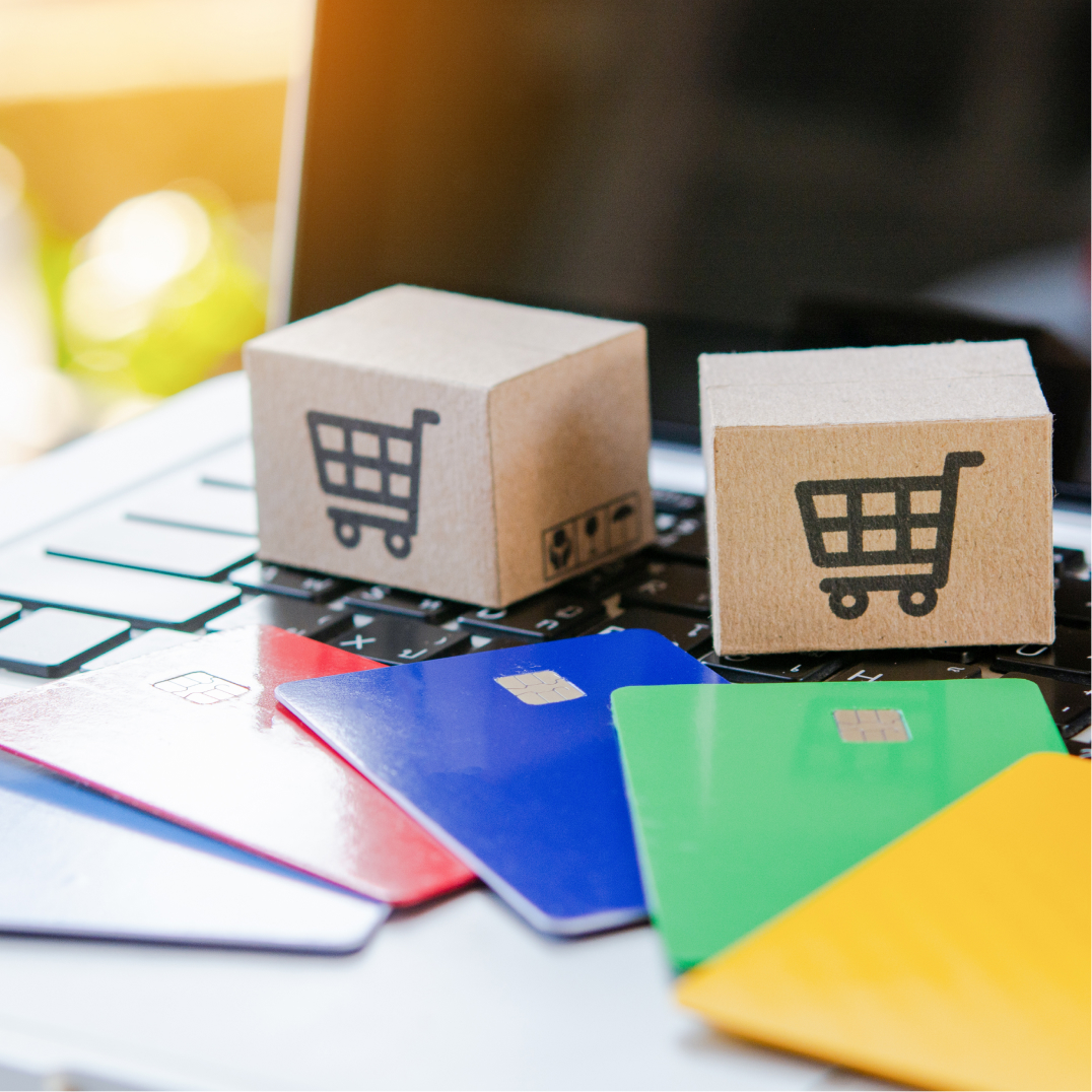 Miniature cardboard shopping boxes and colorful credit cards resting on a laptop keyboard for online shopping.
