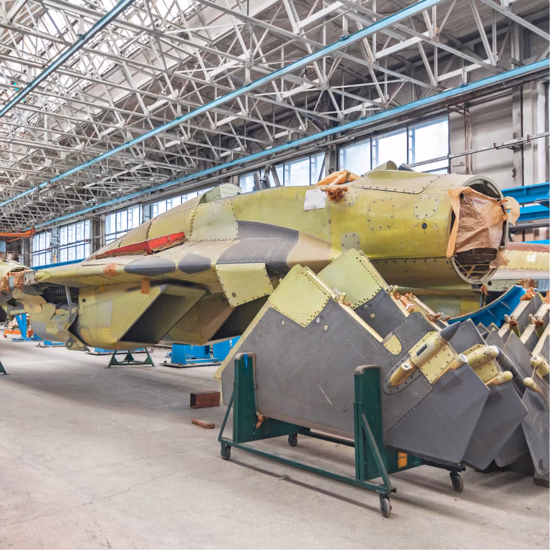 Unfinished aircraft fuselage in yellow primer sits inside a large industrial hangar during aircraft assembly work.