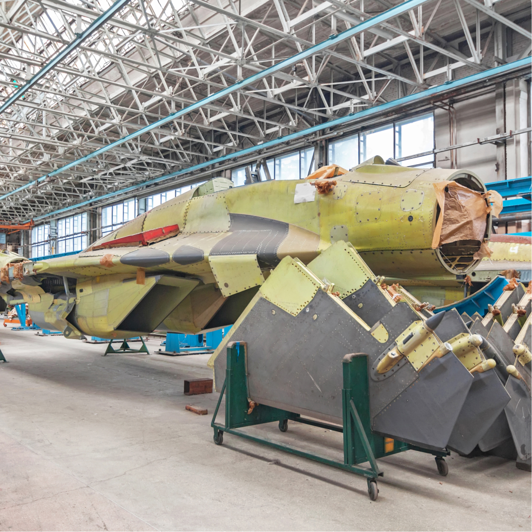 Unfinished aircraft fuselage in yellow primer sits inside a large industrial hangar during aircraft assembly work.