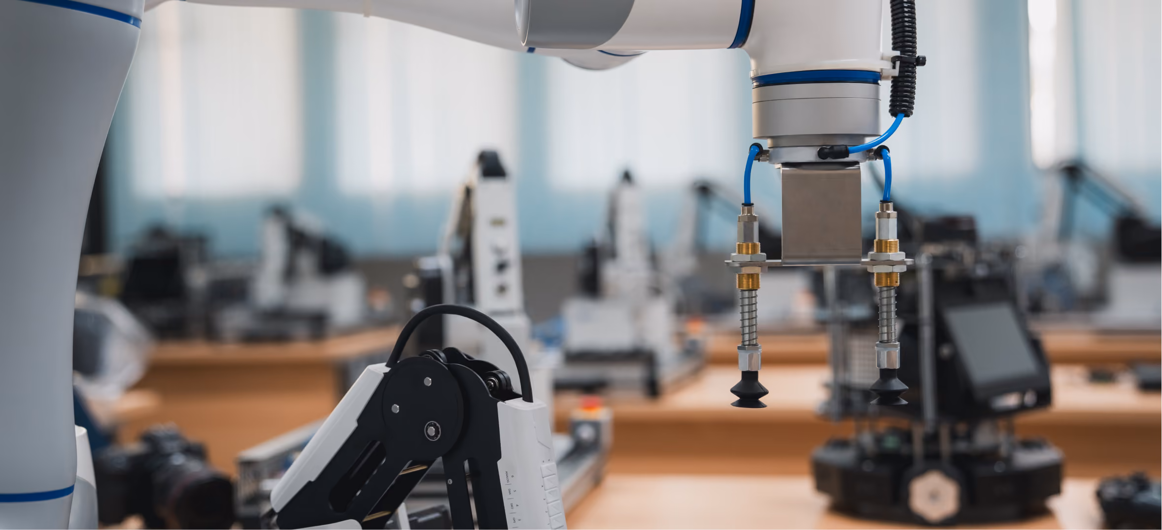 Close-up of a robotic arm with vacuum suction grippers inside a robotics lab filled with automated machines.