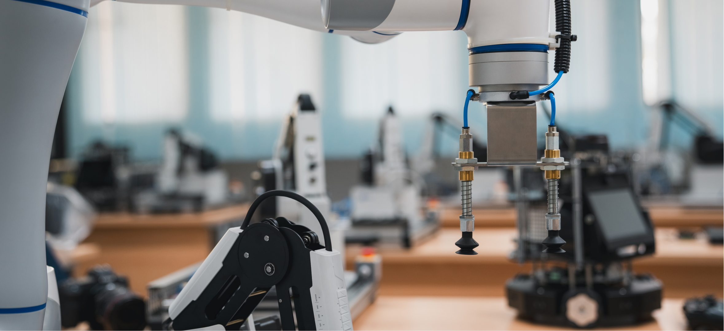Close-up of a robotic arm with vacuum suction grippers inside a robotics lab filled with automated machines.
