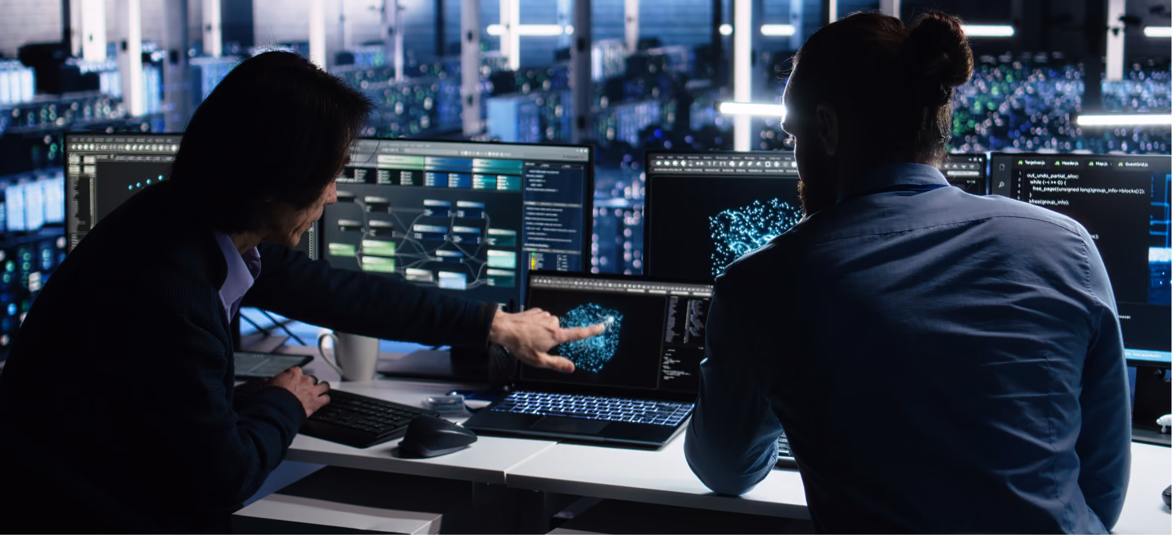 Two silhouetted analysts examine glowing network diagrams and code on multiple monitors in a dark server room.