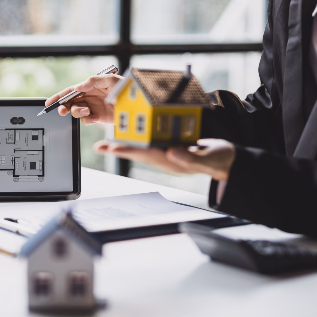Realtor holding small model house beside floor plan, representing Austin real estate development and proptech