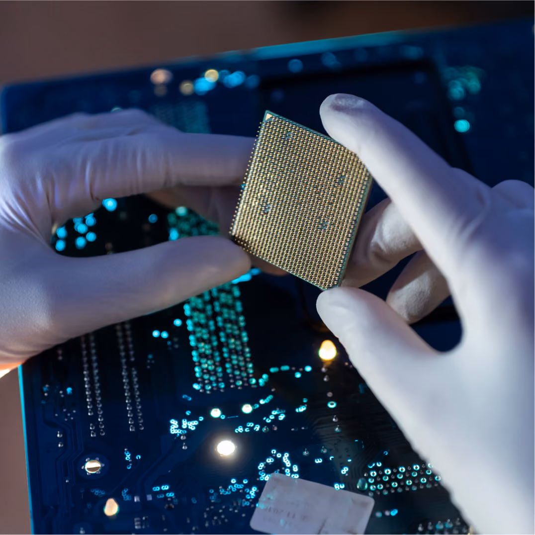 Gloved hands holding microchip over glowing circuit board, representing semiconductor and chip design work