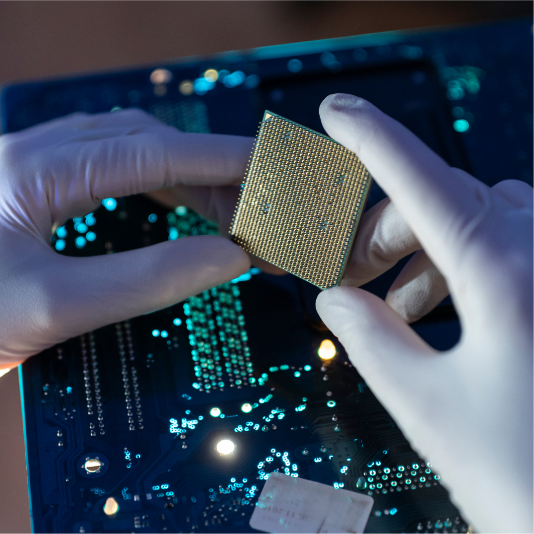 Gloved hands holding microchip over glowing circuit board, representing semiconductor and chip design work