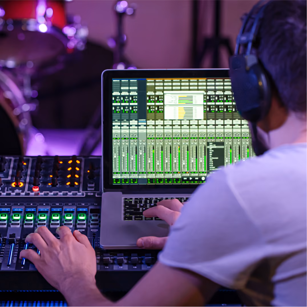 Man mixing audio on laptop near drum kit, representing Austin's music technology and entertainment innovation