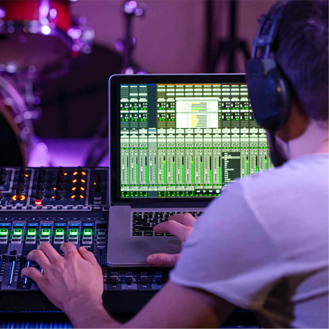 Man mixing audio on laptop near drum kit, representing Austin's music technology and entertainment innovation