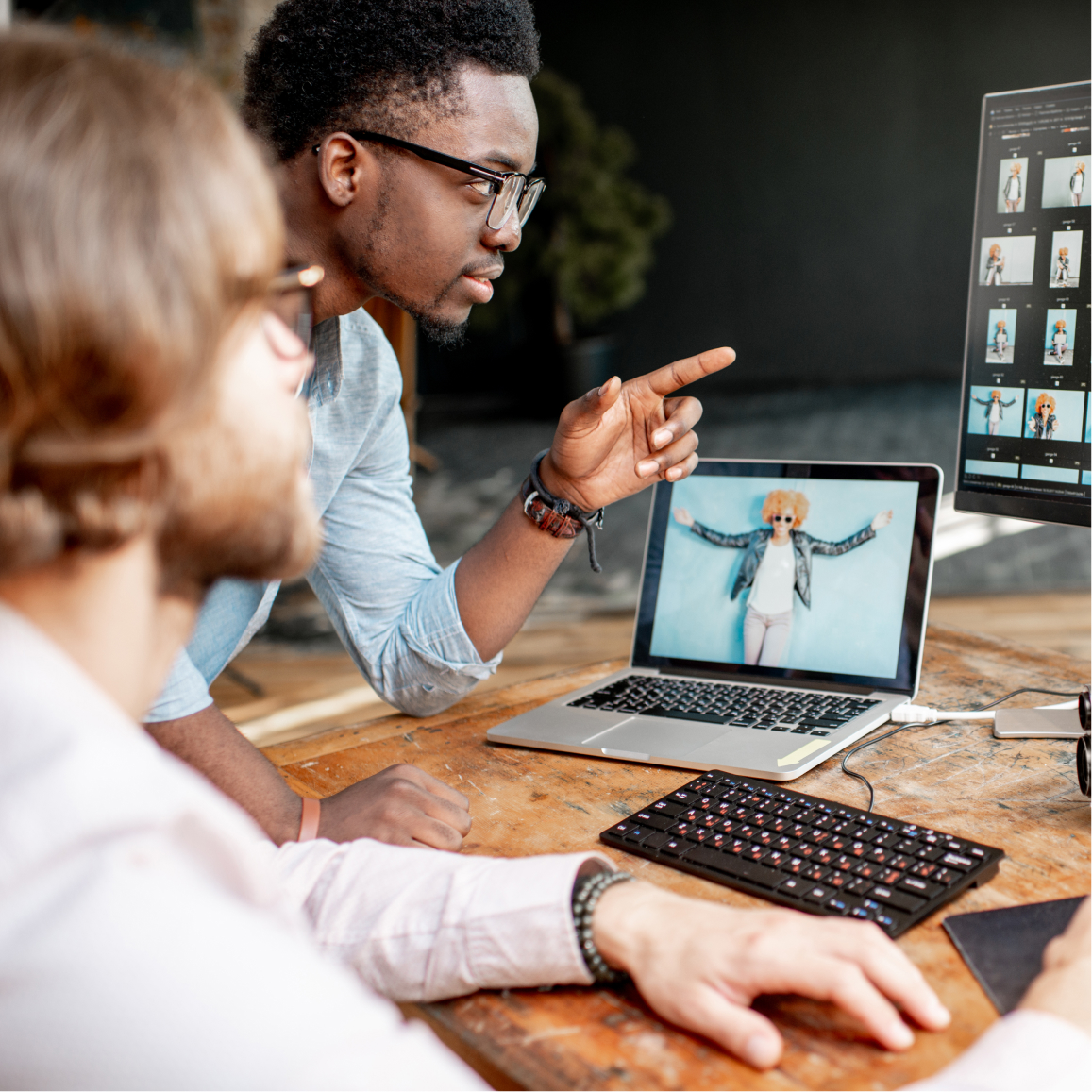 Creative professionals review digital photo edits on desktop monitor and laptop during collaborative design wo