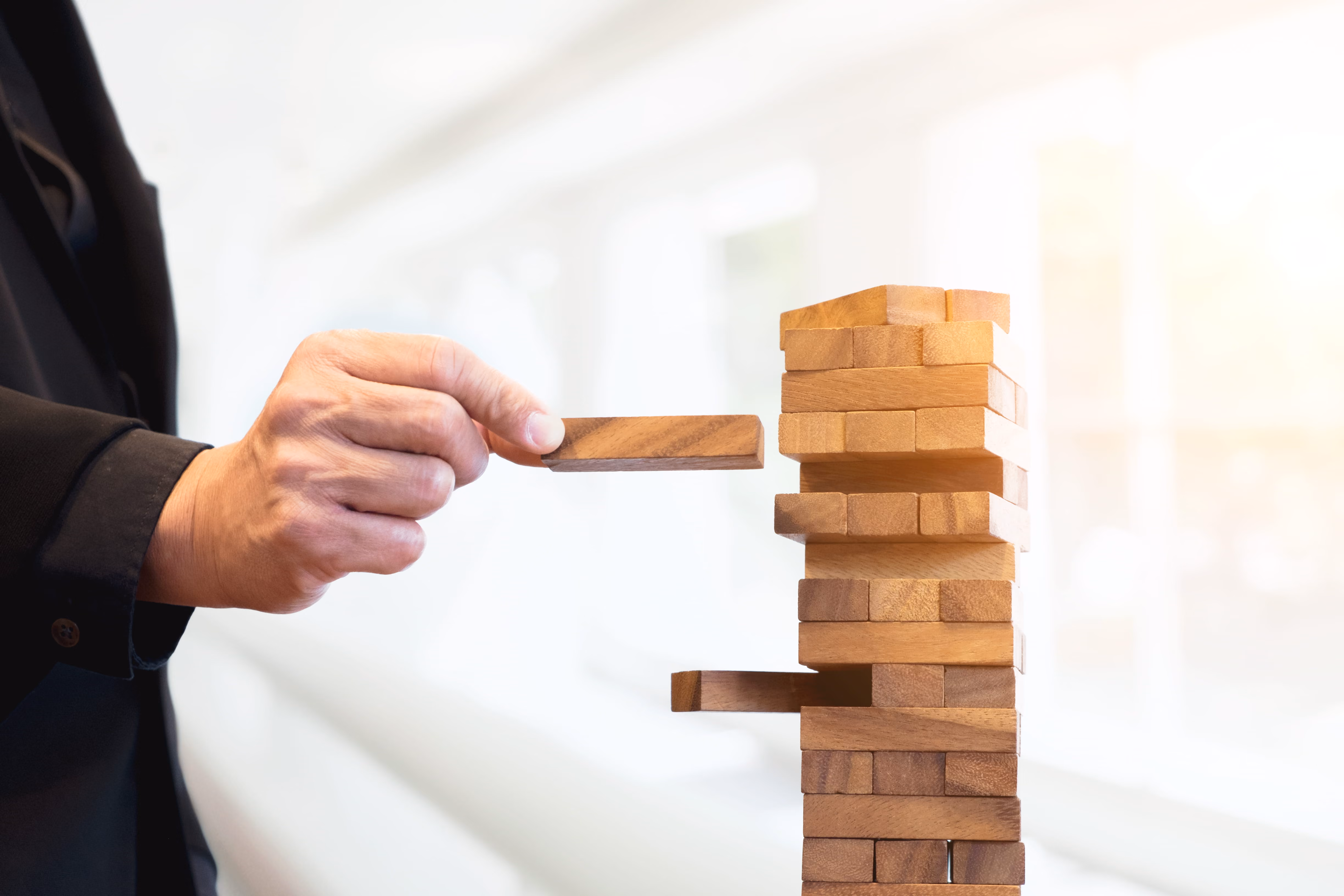 Risk management concept showing hand striking a block tower, representing strategic risks and decision-making.