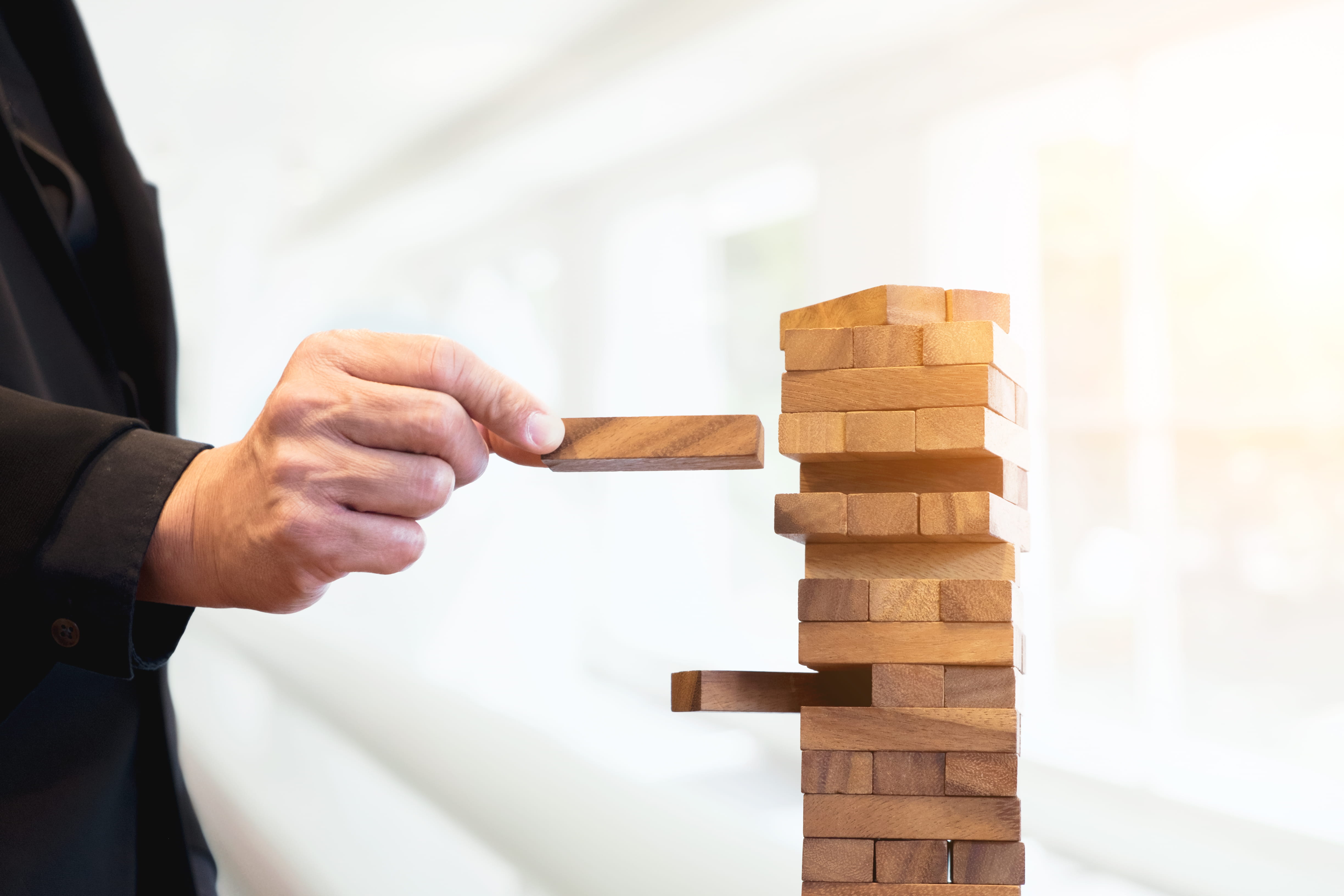 Risk management concept showing hand striking a block tower, representing strategic risks and decision-making.